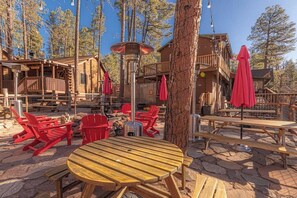 A rustic wooden cabin with outdoor seating, including red chairs and picnic tables, surrounded by trees. - Forest Cabin 3 Bear's Den (Payson)