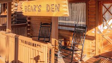 A wooden cabin with a sign reading "BEAR'S DEN" and two rocking chairs on the porch.