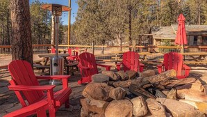 A rustic outdoor seating area with red Adirondack chairs, a fire pit, and a wooden table. - Forest Cabin 3 Bear's Den (Payson)