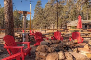 A rustic outdoor seating area with red Adirondack chairs, a fire pit, and a wooden table. - Forest Cabin 3 Bear's Den (Payson)