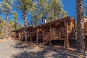 Un bâtiment de style rustique, rappelant une cabane, doté de plusieurs terrasses et d’escaliers en bois, et entouré de grands pins.