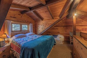 A cozy attic bedroom with a wooden ceiling, a bed with a quilt, a nightstand, a dresser, and a window with curtains. - Forest Cabin 3 Bear's Den (Payson)