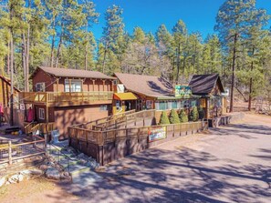 A lodge with multiple wooden buildings, a covered walkway, and a sign indicating 'Mon Serv. 5:00 AM - 9:00 PM'. - Forest Cabin 3 Bear's Den (Payson)
