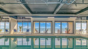 An indoor swimming pool with clear views of the ocean through large windows, surrounded by lounge chairs.