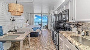A modern kitchen with a large stove, microwave, and stainless steel sink. There is a dining area with a table and chairs, and a balcony with a view of the ocean.