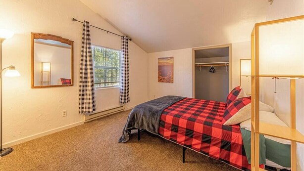 Un dormitorio con cama, armario, espejo y ventana con cortinas.