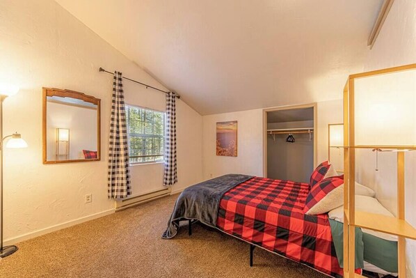 Une chambre à coucher avec un lit, une armoire, un miroir et une fenêtre avec des rideaux.