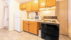 Una cocina con armarios de madera, un refrigerador blanco, un microondas y una estufa negra.