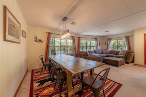 A spacious living room with a wooden dining table, comfortable seating, large windows, and a ceiling light fixture. - Forest Home Retreat 11 Ridgeview Retreat (Payson)