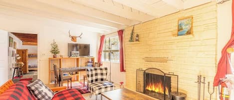 A cozy living room with a fireplace, a checkered sofa, a wooden table, and a bookshelf.