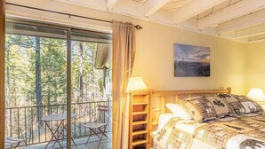 Une chambre à coucher avec un lit, une table de chevet, une lampe, une fenêtre avec un rideau et une vue sur les arbres.