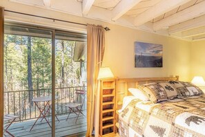 A bedroom with a bed, a nightstand, a lamp, a window with a curtain, and a view of trees. - Forest Home Retreat 11 Ridgeview Retreat (Payson)