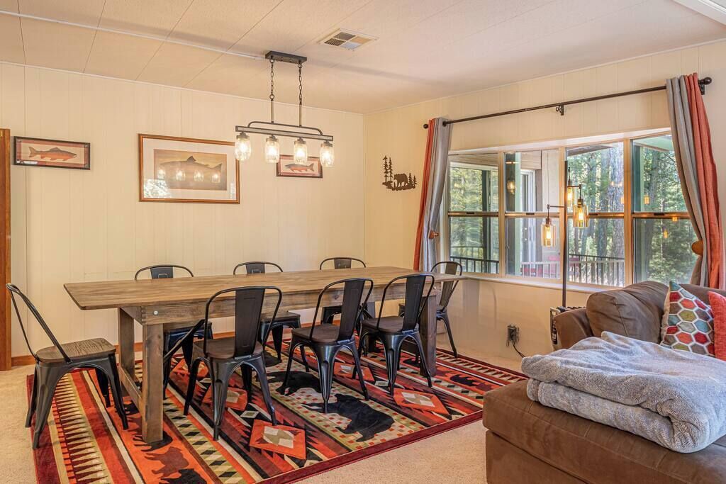 A dining area with a wooden table and chairs, a patterned rug, and a window with curtains.
