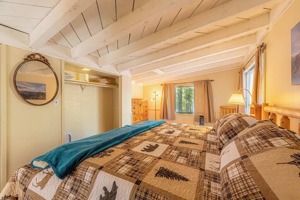 A bedroom with a bed, a mirror, a wardrobe, and a window with curtains.