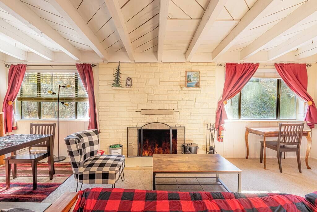 A cozy room with a fireplace, wooden furniture, and large windows with curtains.