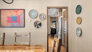 A dining area with a wooden table and chairs, a large abstract painting, and several decorative plates on the wall.