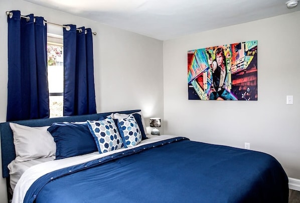A bedroom with a bed, blue curtains, and a colorful painting on the wall.