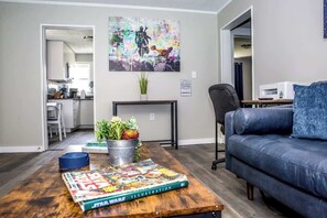 A living room with a dark blue sofa, a coffee table with a Star Wars magazine, a colorful abstract painting, and a kitchen visible through an open doorway.