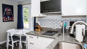 A compact kitchen with white cabinets, a microwave, a sink, and a small dining area with a white table and chairs. - "Rebel Base" in the  Heart of Fayetteville (Fayetteville)