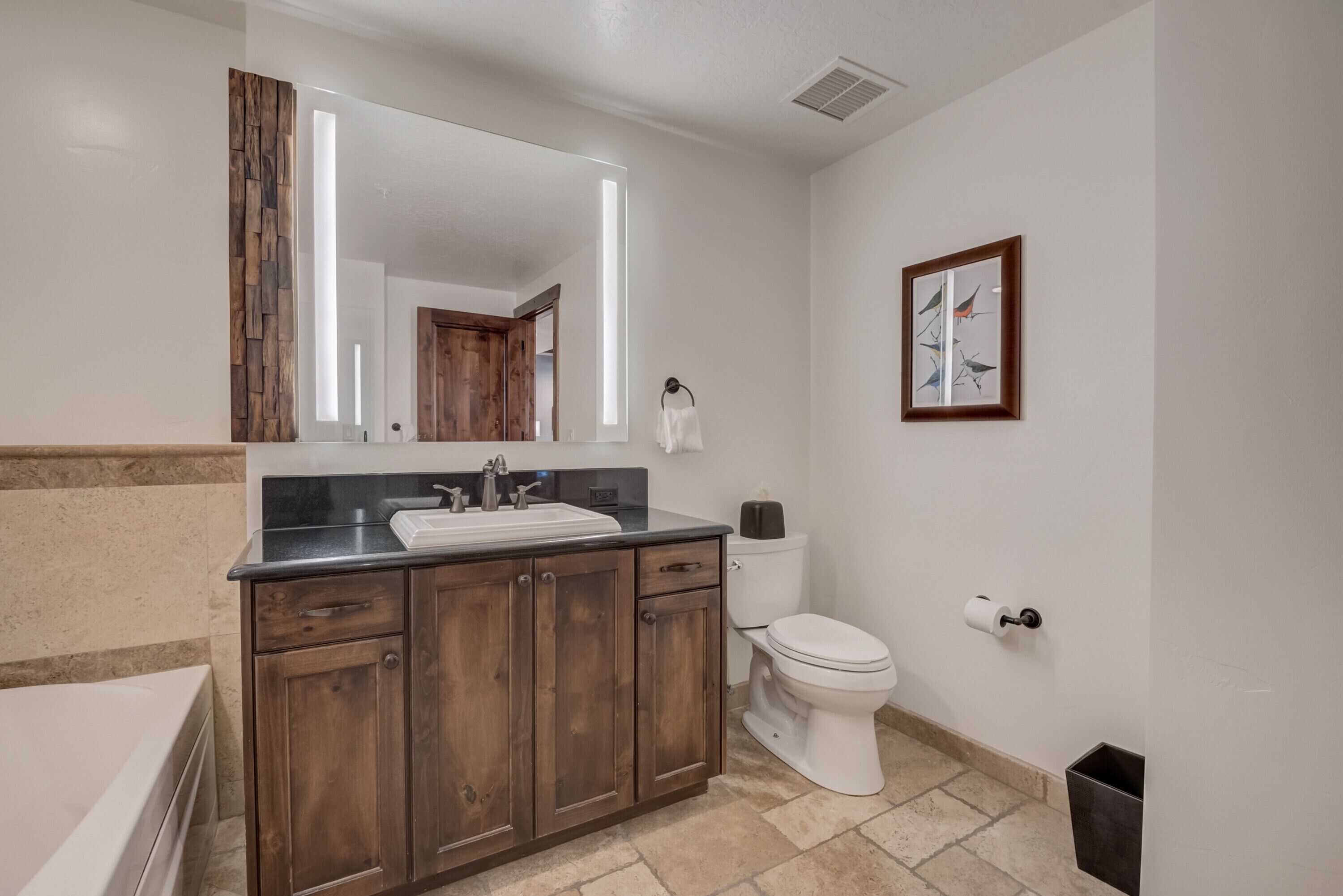 A bathroom with a wooden vanity, a sink, a toilet, and a framed picture on the wall.
