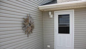 A room with horizontal siding, a white door, and a wall-mounted light fixture. - Spectacular beachfront with epic views, beautiful lit-up deck for sunset dining! (Lubec)