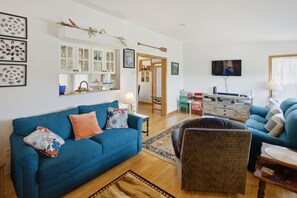 A living room with a blue sofa, a wooden coffee table, a television, and a kitchen area in the background.