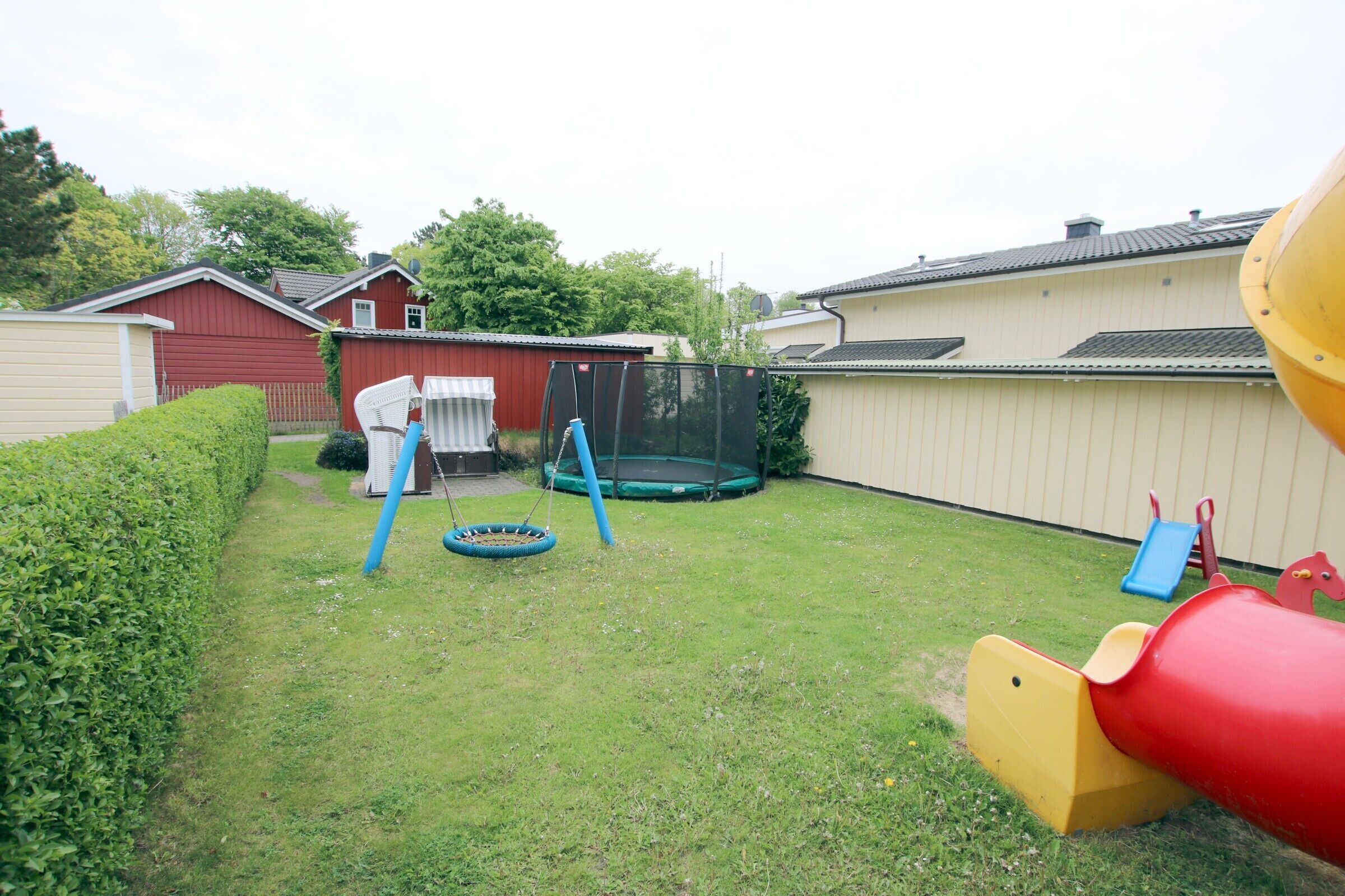 Un jardin avec un trampoline, une balançoire et un toboggan.