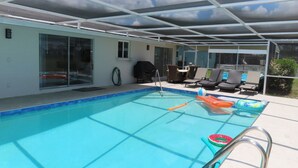 Ein Schwimmbad mit Glasveranda, eine überdachte Terrasse mit Liegestühlen und ein klarer Himmel.
