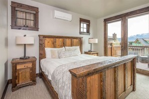 A bedroom with a wooden bed, two bedside tables, and a large window offering a view of a mountain.
