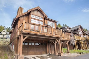 A large wooden house with a prominent balcony, multiple windows, and a garage.