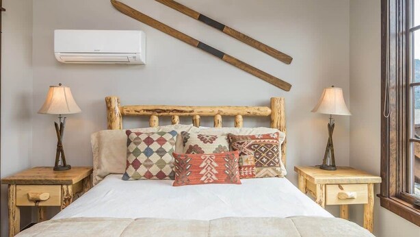Una camera da letto con una testiera in legno, diversi cuscini decorati, lampade da comodino e un condizionatore d'aria a parete.