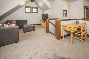 A loft-style living space with a gray sofa, ottoman, and wooden dining table.