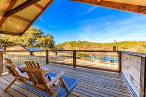 A wooden deck with two Adirondack chairs, a view of a golf course, and a building in the distance. - Lakefront Hill Country Glamping | Hot Tub + River (Hunt)