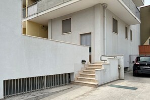 A modern building with a staircase leading to a second floor, a car parked outside, and a metal fence.