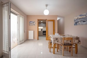 Comedor con una mesa dispuesta para cuatro, un radiador y vista a la cocina a través de una puerta abierta.