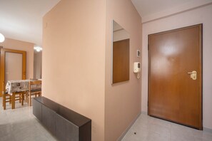 A hallway with a wooden door, a mirror, a phone, a bench, and a dining area with chairs and a table. - WePuglia - Appartamento Sibilla (Monopoli)