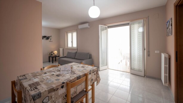 Ein Essbereich mit Tisch für zwei Personen, einer Couch und einer Glastür zum Balkon.
