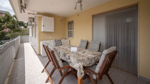 Ein überdachter Essbereich im Freien mit Tisch und Stühlen, einem weißen Schrank und einem Fenster.
