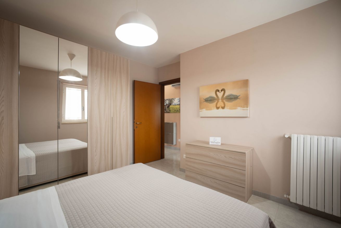 Quarto com cama, cômoda, espelho, pintura e radiador.