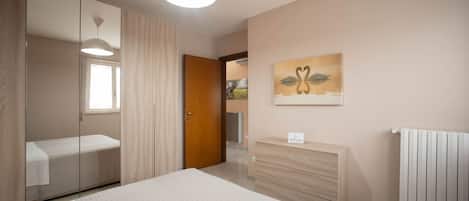 A bedroom with a bed, a dresser, a mirror, a painting, and a radiator.