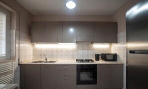 A modern kitchen with grey cabinets, a stainless steel refrigerator, a microwave, and a gas stove.