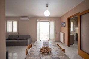 Un coin repas avec une table dressée pour quatre personnes, un bol de collations, un canapé et une vue sur l’extérieur.