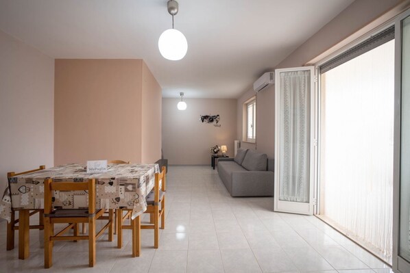 Un coin repas avec une table et des chaises, un canapé, une petite table avec une lampe et une porte-fenêtre coulissante donnant sur un balcon.