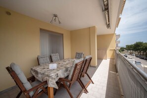 A balcony with a table and chairs, a window with blinds, and a view of the street. - WePuglia - Appartamento Sibilla (Monopoli)