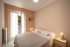 Une chambre à coucher avec un lit, une table de chevet avec une lampe, un tableau au mur et une porte donnant sur un espace extérieur.