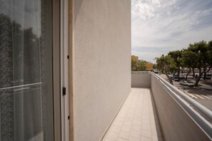 A balcony with a tiled floor, a glass door, and a view of a street with cars and trees.