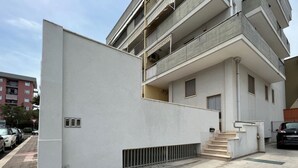 Ein modernes Mehrfamilienhaus mit weißer Fassade, mehreren Balkonen und einer sichtbaren Treppe, die zum Eingang führt.