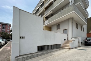 Un edificio moderno de apartamentos con fachada blanca, varios balcones y una escalera visible que lleva a la entrada.