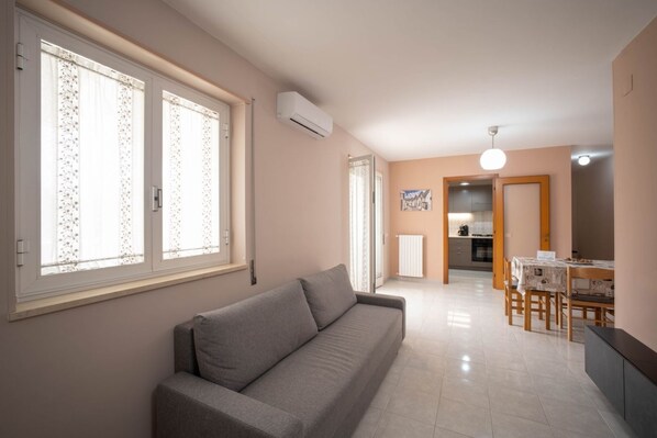 A living room with a sofa, a dining area with a table and chairs, and a kitchen in the background.
