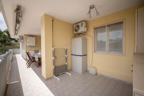 A balcony with a table and chairs, a clothes drying rack, a refrigerator, and an air conditioning unit.
